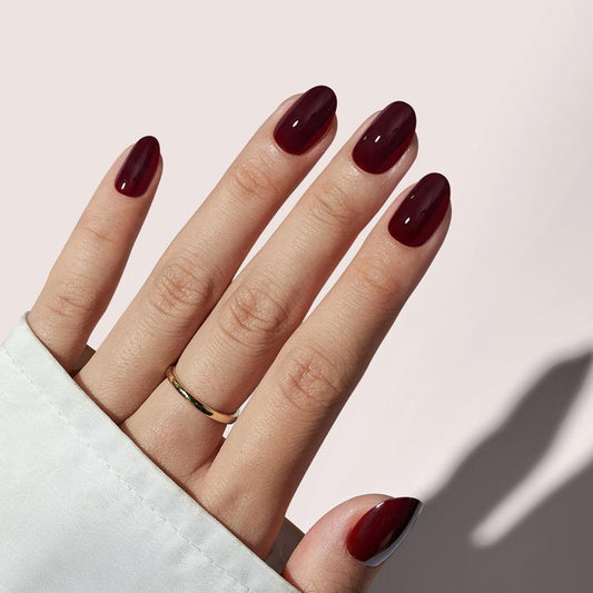 Hand with dark red nail polish on a light pink background