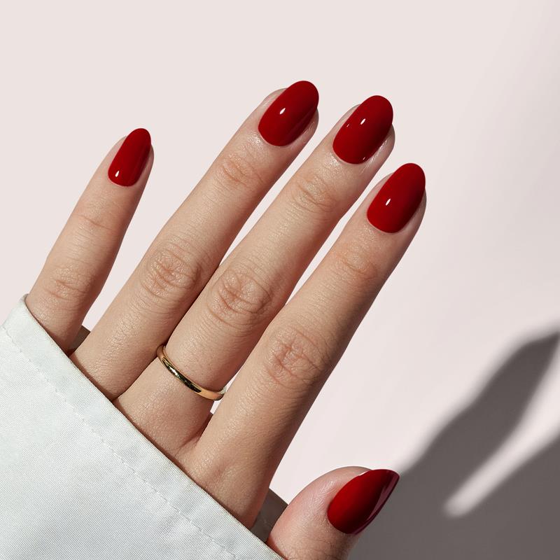 Hand with red nail polish on a light pink background