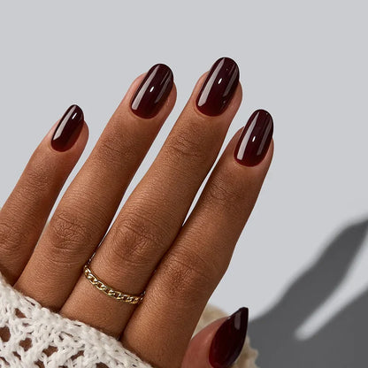 Hand with dark red nail polish on a light gray background