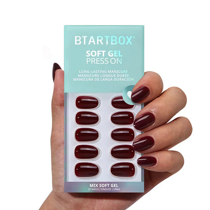 Hand holding a BTARTBOX soft gel press-on nail set with dark red nails.