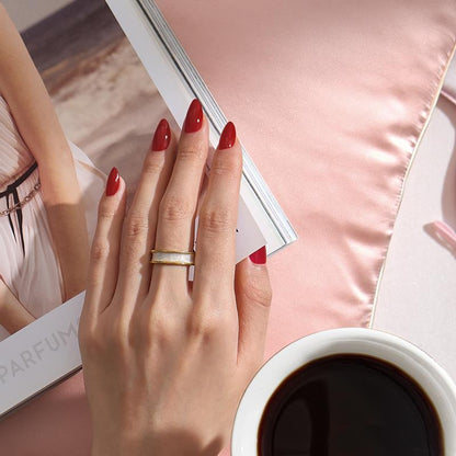 Hand with red nail polish and a ring, holding a magazine with a coffee cup in the foreground.