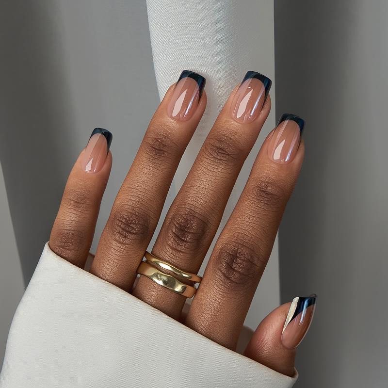 Close-up of a hand with manicured nails and a gold ring on a neutral background